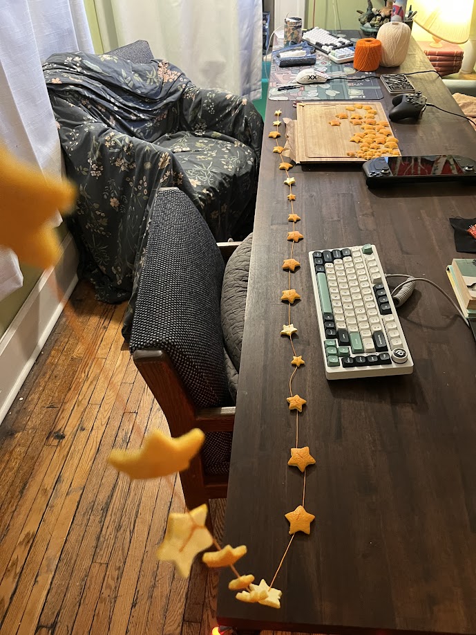 An orange garland in the midst of creation; star-shaped orange peels are being strung up at intervals on an orange thread.