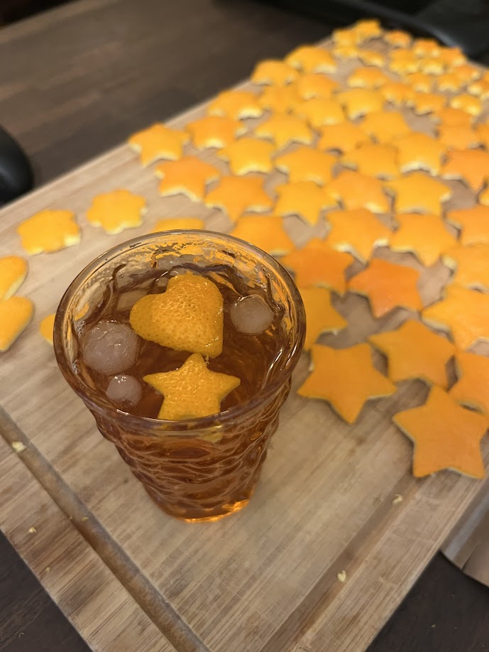 Cookie-cuttered oranges on a cutting board; some have been used as garnish in an old fashioned.